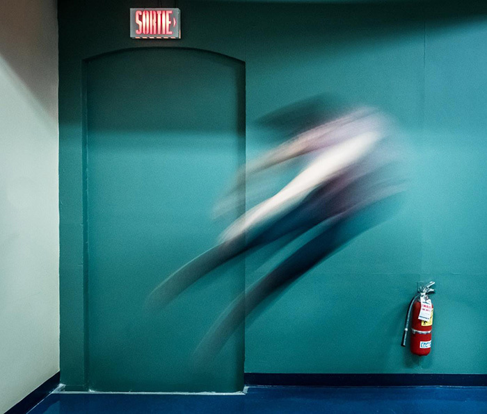 A blured person jumping backwards in a hallway near an emergency exit and a fire extinguisher